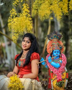 a woman sitting on the ground next to a statue of a hindu god in front of yellow flowers