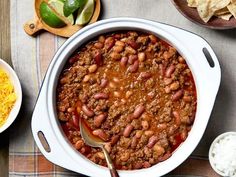 chili and beans in a white bowl next to nachos, sour cream and lime