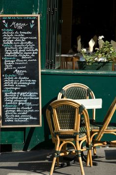 two chairs and a table in front of a green building with menus on it