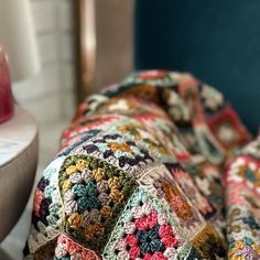 a crocheted blanket sitting on top of a bed next to a vase and lamp