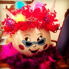 a pumpkin decorated with colorful feathers and a tiara on it's head is sitting on a table