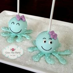 two blue cake pops decorated like octopuses with pink bows on them sitting in ice