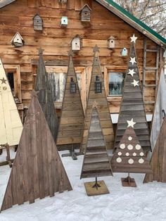 several wooden christmas trees in front of a building with snow on the ground around them