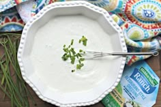 a white bowl filled with ranch dressing and topped with chives on top of a wooden table