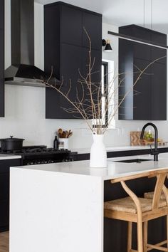 a kitchen with black cabinets and white countertops is pictured in this image, there are two bar stools at the center of the island