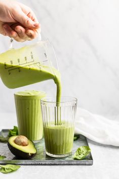 someone pouring green smoothie into a glass with an avocado on the side