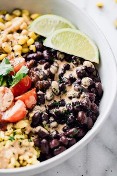 a white bowl filled with black beans, corn, and lime wedges on top of a marble table