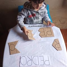 a young boy sitting at a table with cut out letters