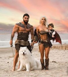 a man and woman in costume walking on the beach with a dog next to them