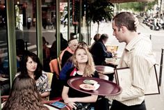 a man standing in front of a group of people sitting at tables talking to each other