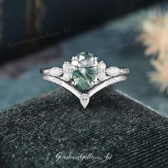 a green and white diamond ring sitting on top of a velvet box