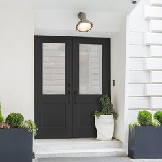 two planters with plants on the steps in front of a door that is painted black