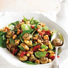 a white bowl filled with spinach, mushrooms and other vegetables next to a spoon