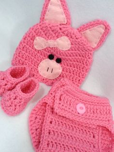 a pink crocheted baby outfit and booties with a stuffed animal on top