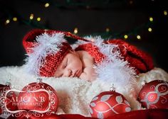 a newborn baby wearing a santa hat and sleeping next to christmas ornaments