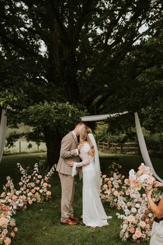 a bride and groom kissing in front of an outdoor ceremony arch with flowers on it