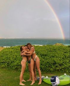 three women hugging each other in front of the ocean with a rainbow in the background