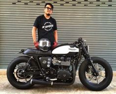 a man standing next to a motorcycle in front of a garage door with his hand on the seat