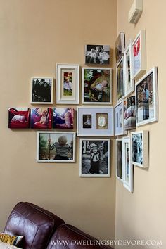 a living room wall filled with pictures and framed photos on the wall next to a brown leather couch