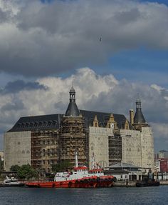 a red and white boat in the water next to a large building with two towers