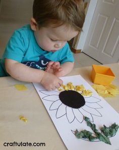 a young boy sitting at a table making a paper sunflower with leaves on it