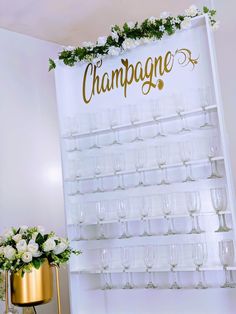 champagne glasses are on display in front of a wine rack with flowers and greenery