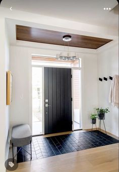 an entryway with a black door and white walls, wooden flooring and potted plants