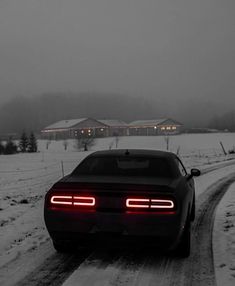 a car driving down a snow covered road in the middle of winter with its lights on