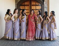 a group of women standing next to each other in front of a door wearing sari