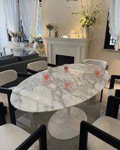 a marble dining table with white chairs and candles on it in front of a fireplace