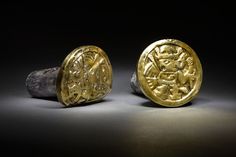 two gold coins sitting next to each other on top of a black surface with a rock in the foreground