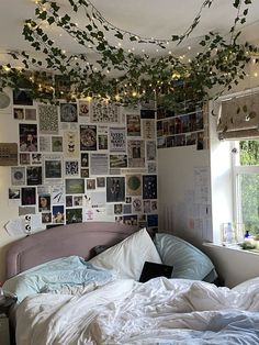 an unmade bed with lots of pictures on the wall and lights hanging from the ceiling