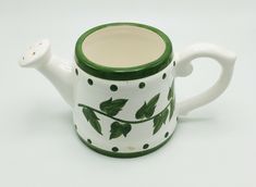 a green and white ceramic teapot with leaves on it's side, sitting on a white surface