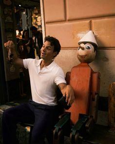 a man sitting on top of a wooden bench next to a puppet