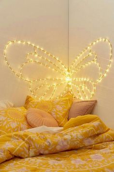 a bed with yellow comforter and lights on the headboard, in front of a white wall