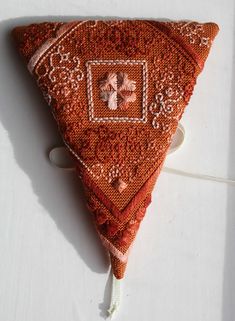 a triangle shaped piece of cloth with an embroidered design on the front and side, sitting on a white surface