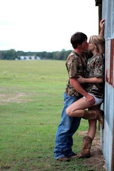 a man and woman kissing in front of a barn