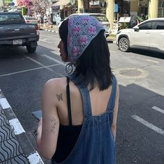 a woman in overalls is standing on the side of the road with her back to the camera