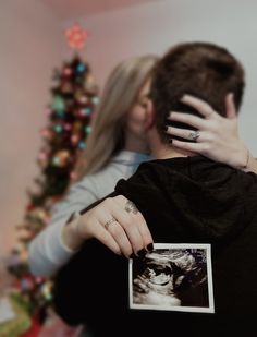 a man and woman embracing each other in front of a christmas tree