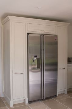 a stainless steel refrigerator in a kitchen with white cabinets and tile flooring on the walls