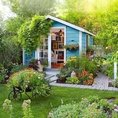 a small blue shed with flowers in the yard