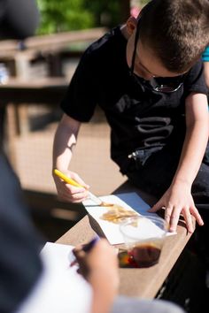 a young boy sitting at a table with food in front of him and another person standing behind him