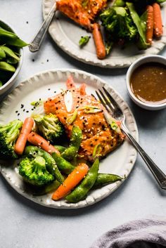 two plates with salmon, broccoli and carrots on them next to some dipping sauce