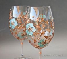 two wine glasses decorated with blue flowers and gold leafy stemings, one is empty