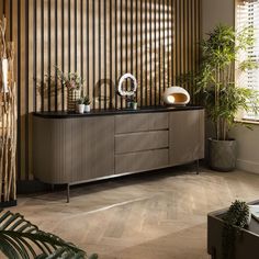 a living room filled with furniture and lots of plants on top of the sideboard