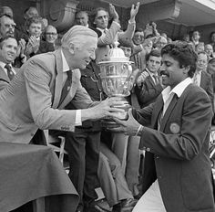 an old photo of two men shaking hands with a trophy in front of a crowd