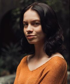 a woman with dark hair wearing an orange sweater