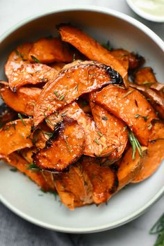 a white bowl filled with cooked carrots on top of a table next to sauce