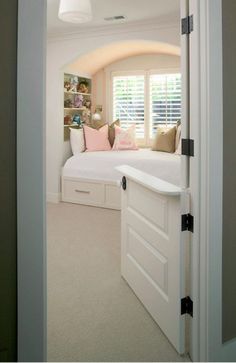 an open door leading to a bedroom with white furniture and pillows on the window sill