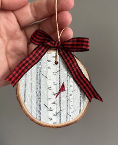 a hand holding a wooden ornament with a red and black ribbon